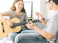 a woman playing guitar sitting in front of her partner